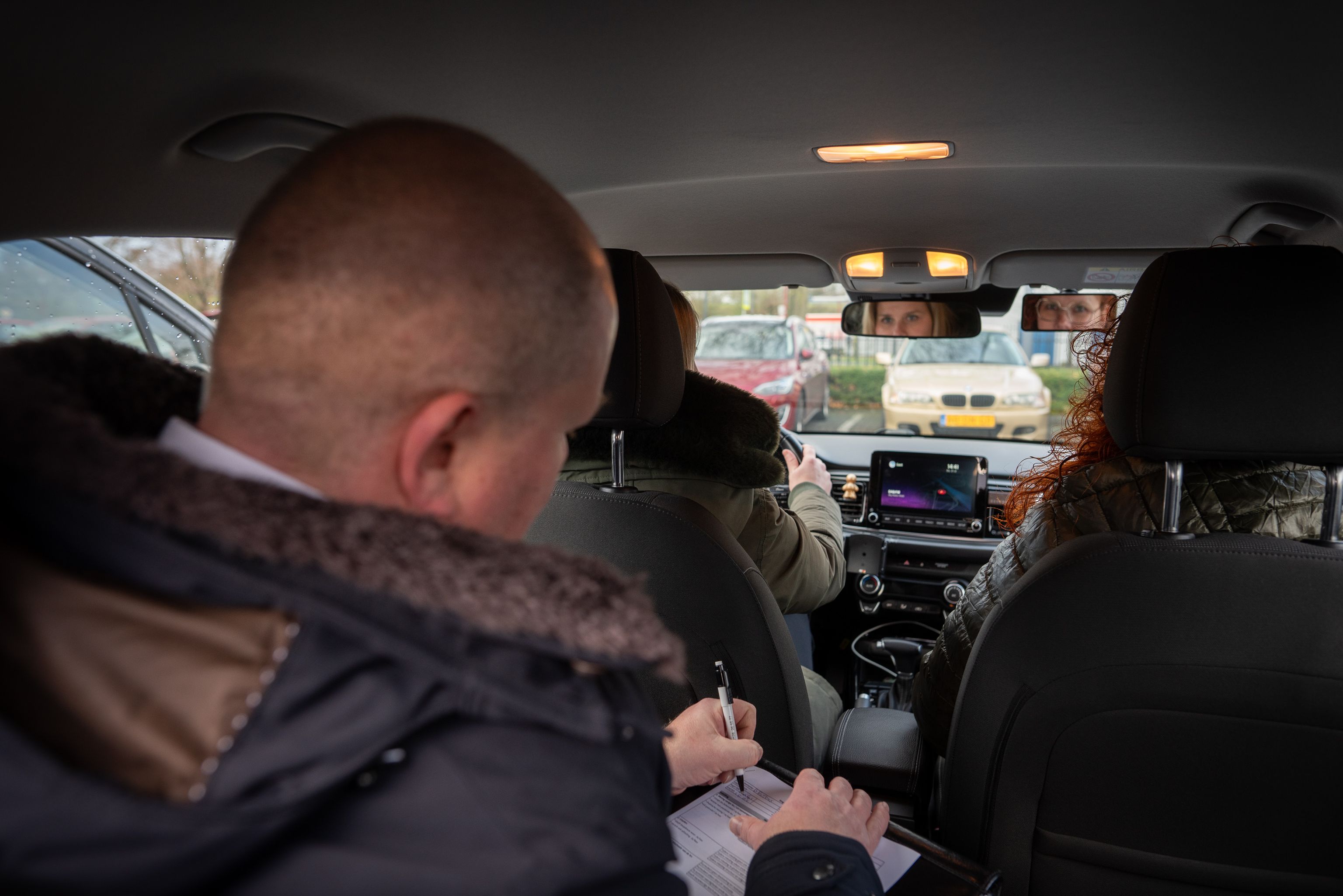 Drie personen in een auto. De persoon achterin heeft een pen in de hand waarmee hij schrijft.