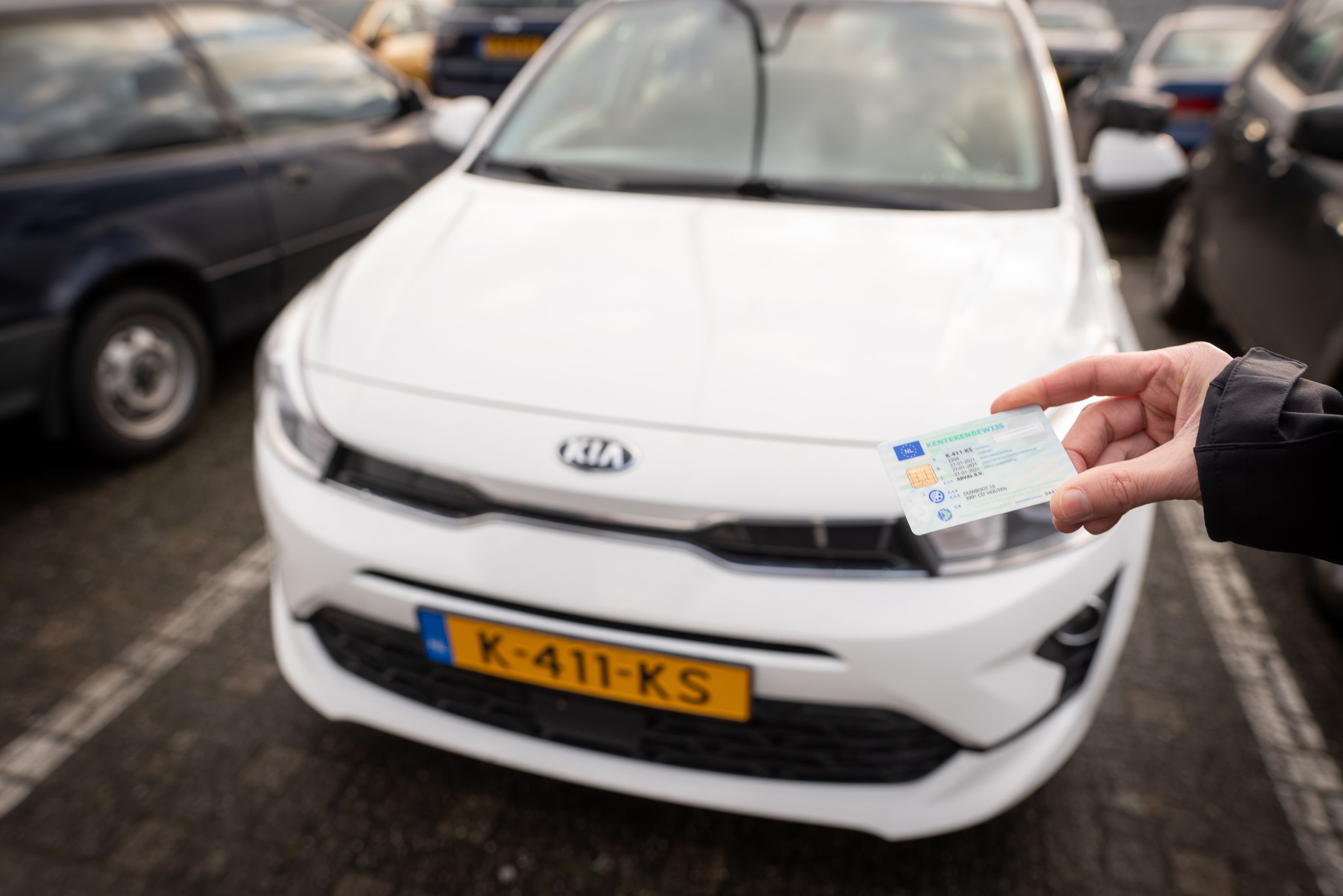 Een hand met daarin een kentekenbewijs dat bij een auto gehouden wordt ter controle.