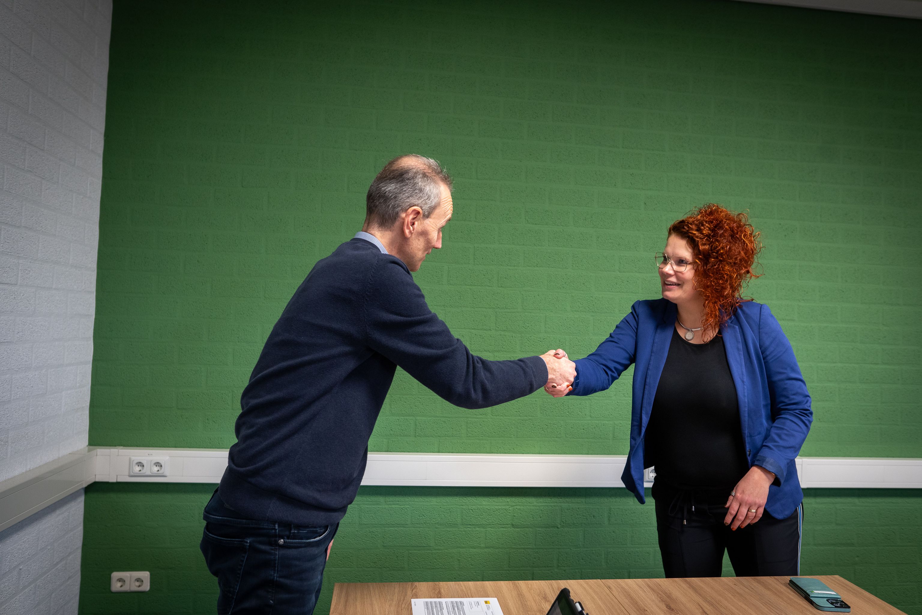 Voor een groene muur geven twee personen elkaar een hand.