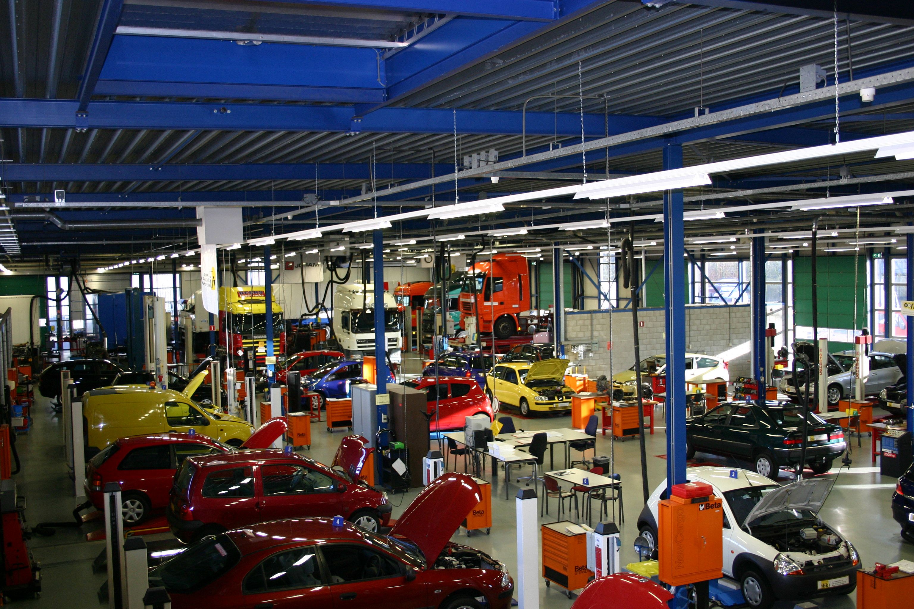 De examenhal met personenauto's, voornamelijk rode. Op de achtergrond staan vrachtauto's.