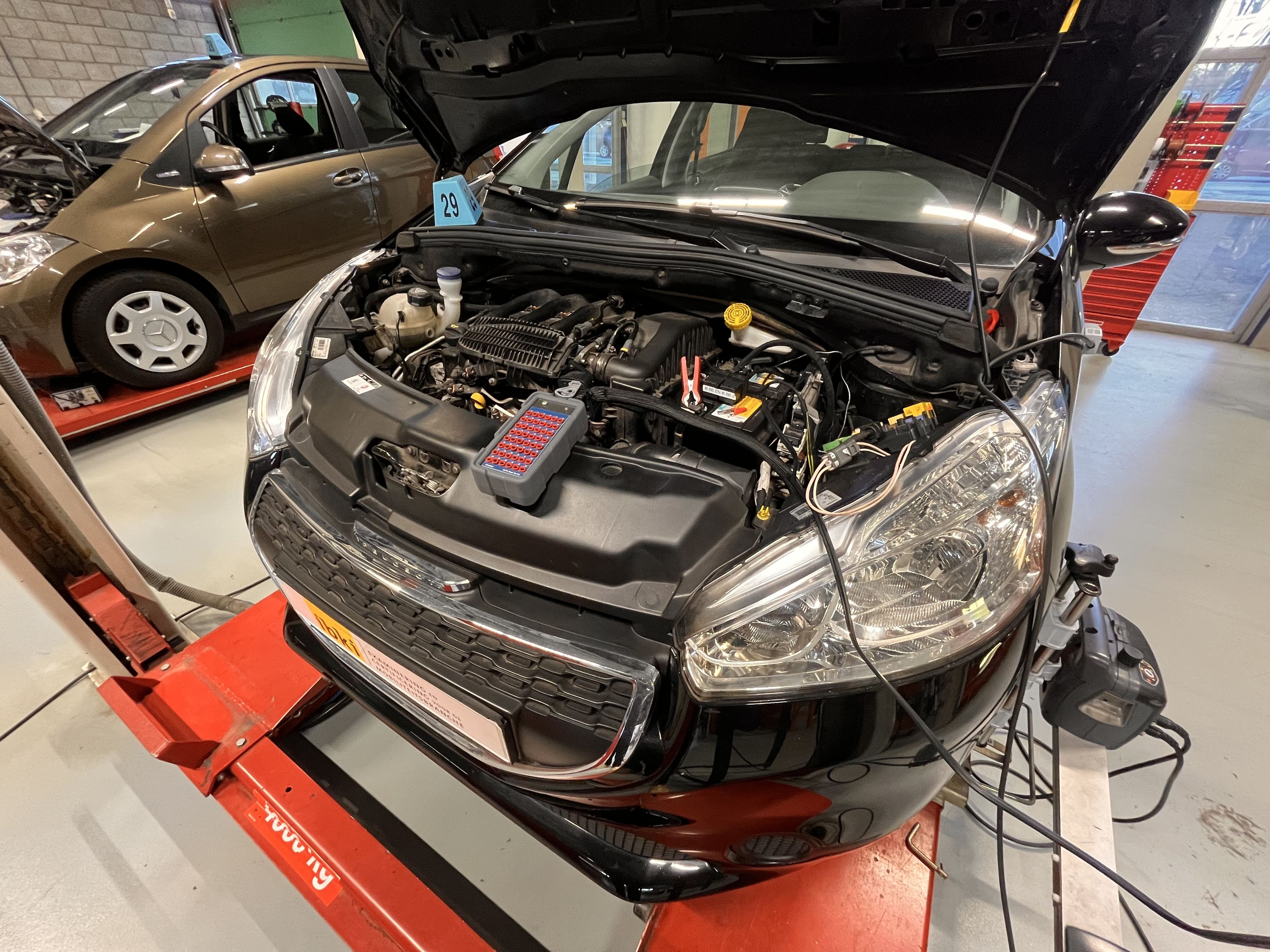 De motor van een personenauto met nummer 29. De motorkap staat open. Er staat een andere personenauto naast.