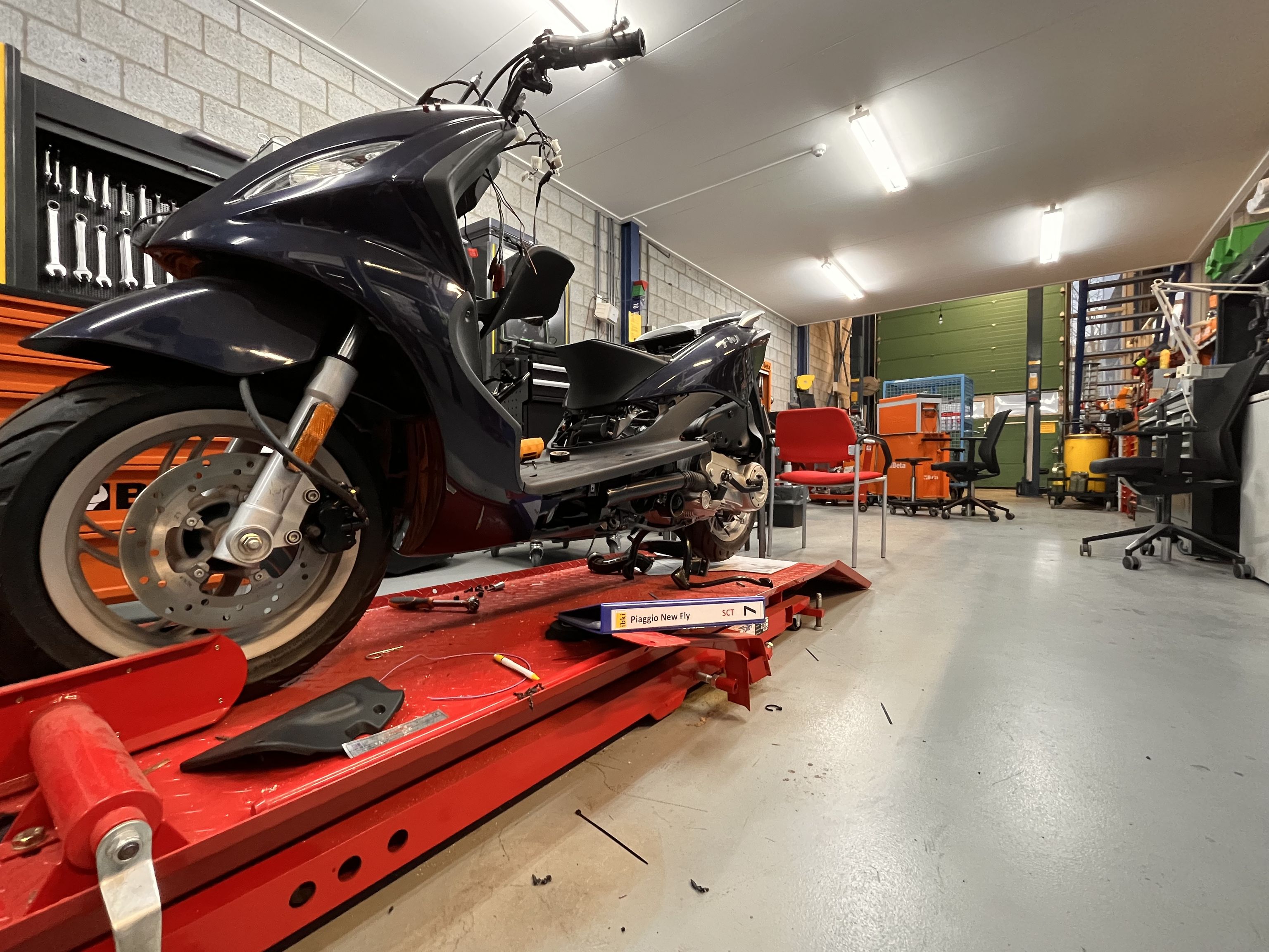 Een opstelling met een scooter om aan te sleutelen. op de achtergrond wat stoelen.