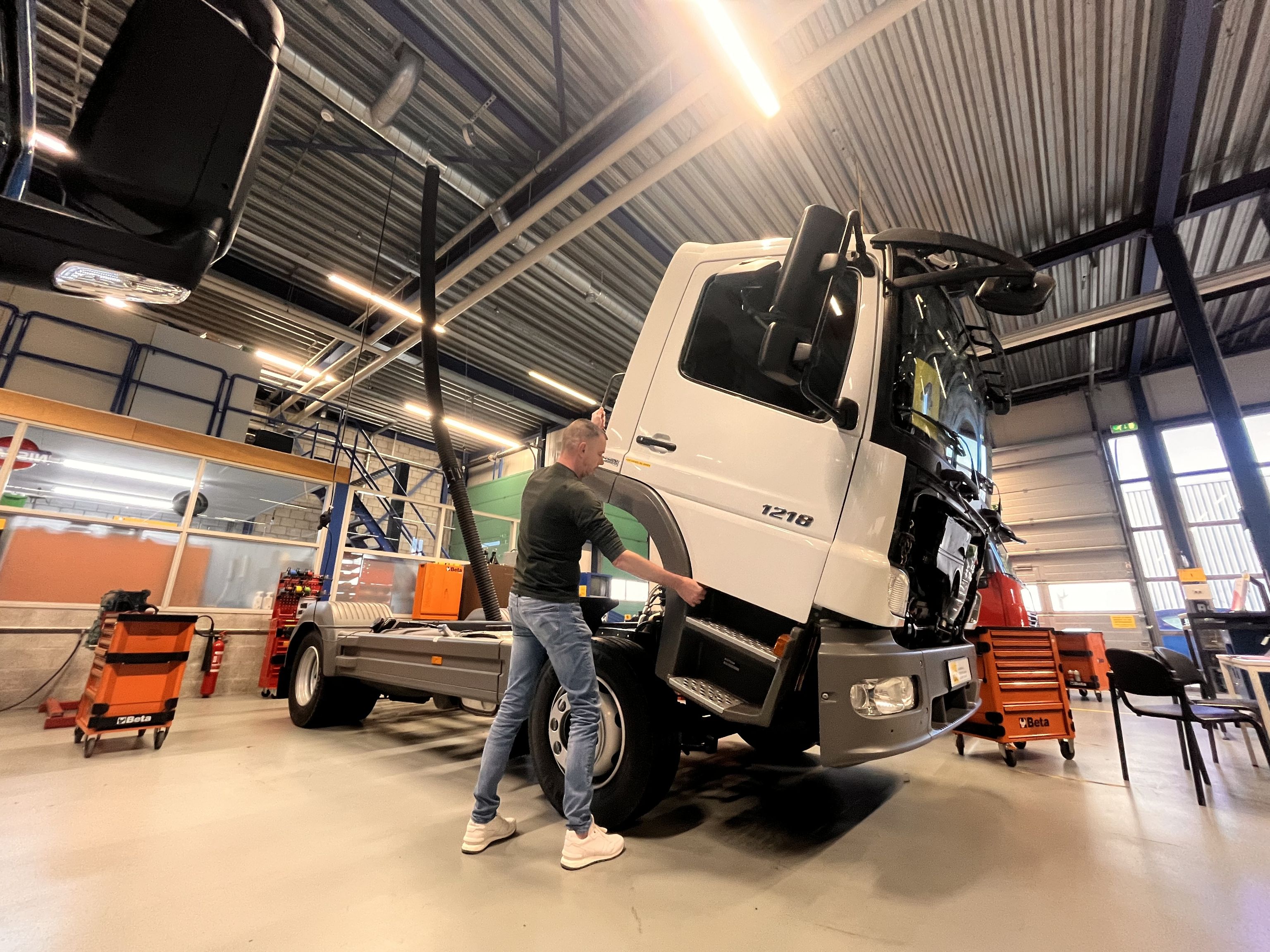 De cabine van een vrachtauto die gekanteld wordt door een persoon. Er staan gereedschapskarren omheen.