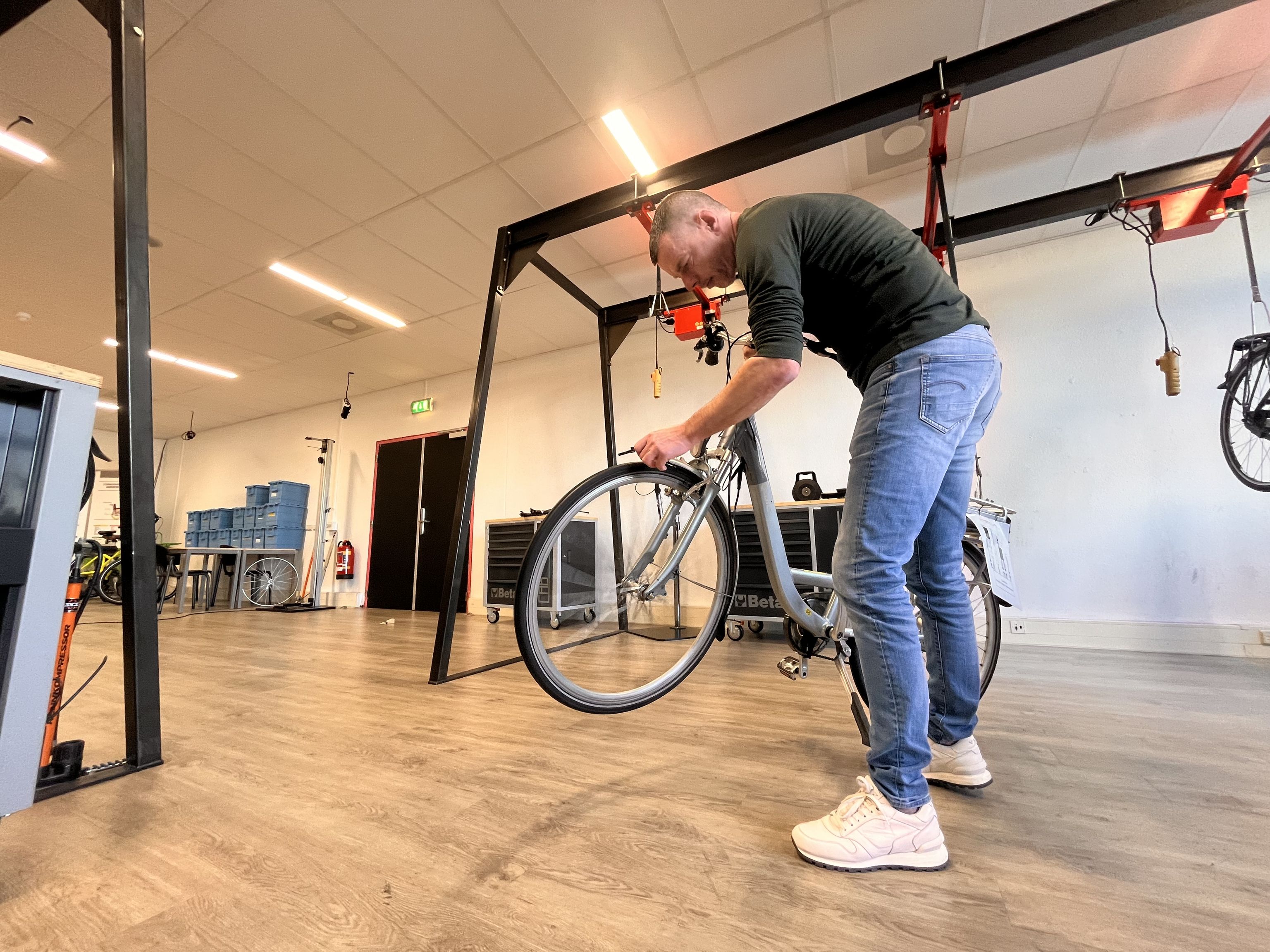 Een man checkt een fiets in een lokaal. Op de achtergrond staat een gereedschapskar.
