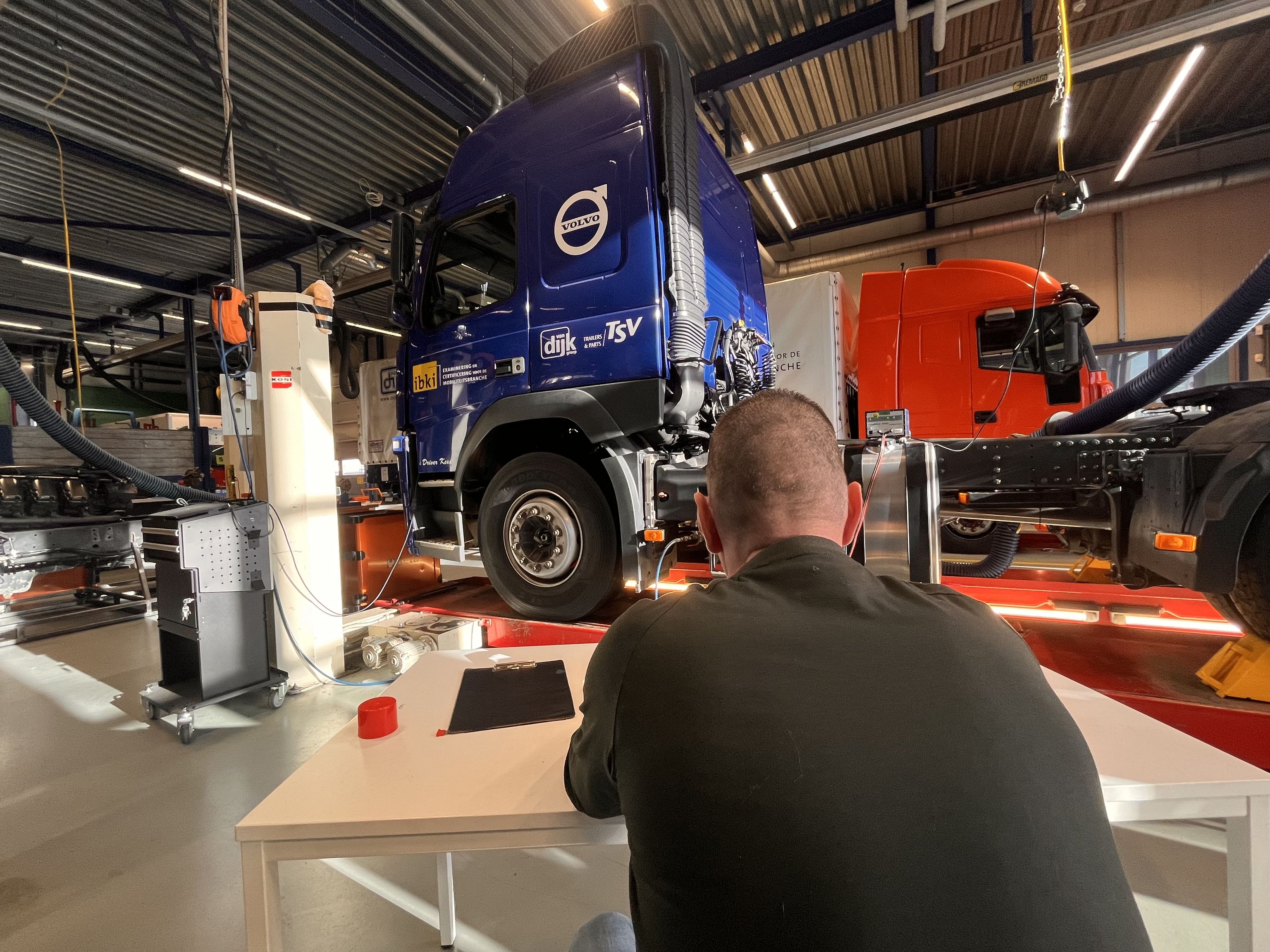 Achterkant van een deelnemer aan een tafel met op de achtergrond vrachtauto's.