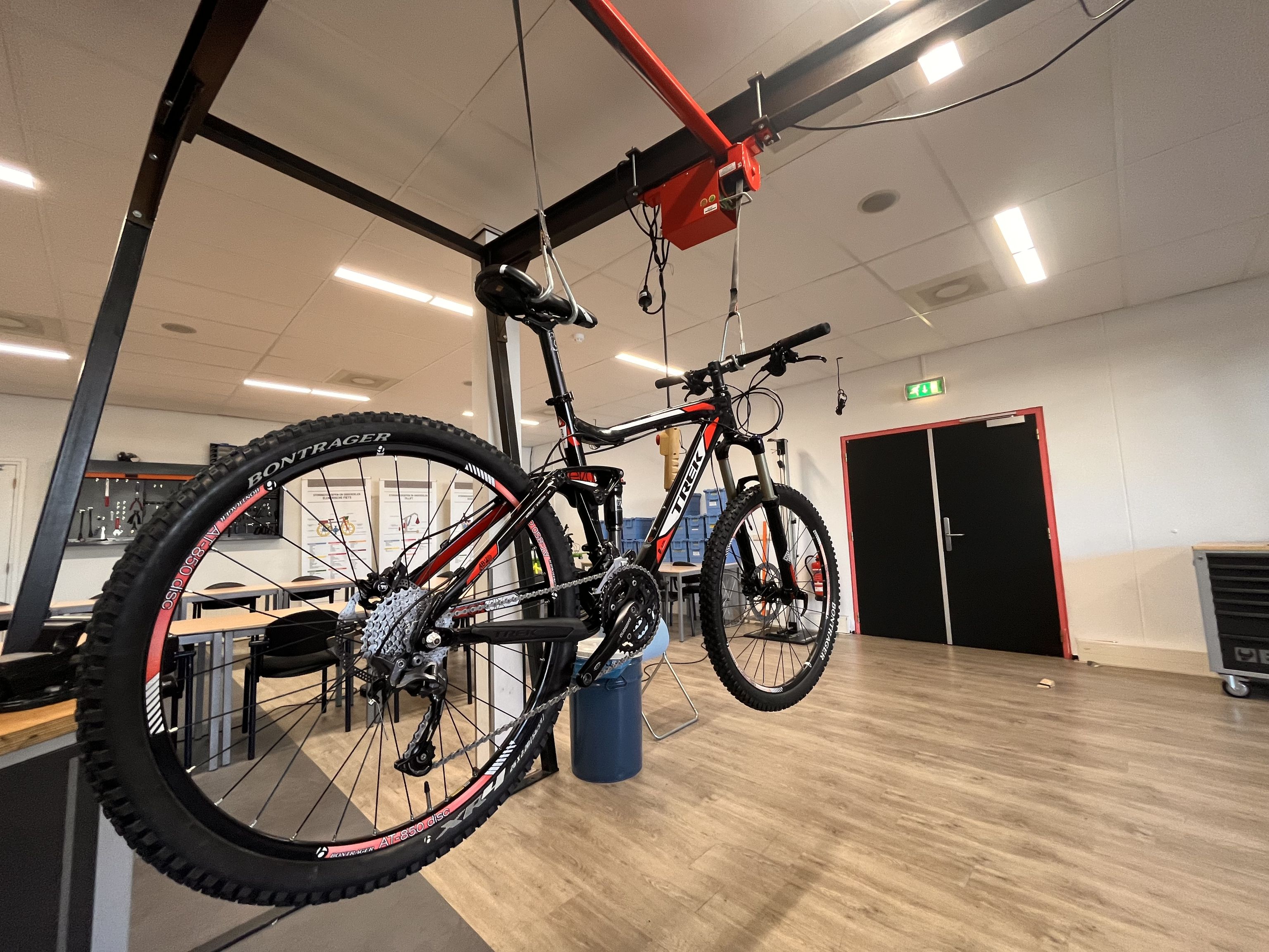 Een fiets die opgehangen is in een lokaal met tafels en stoelen.