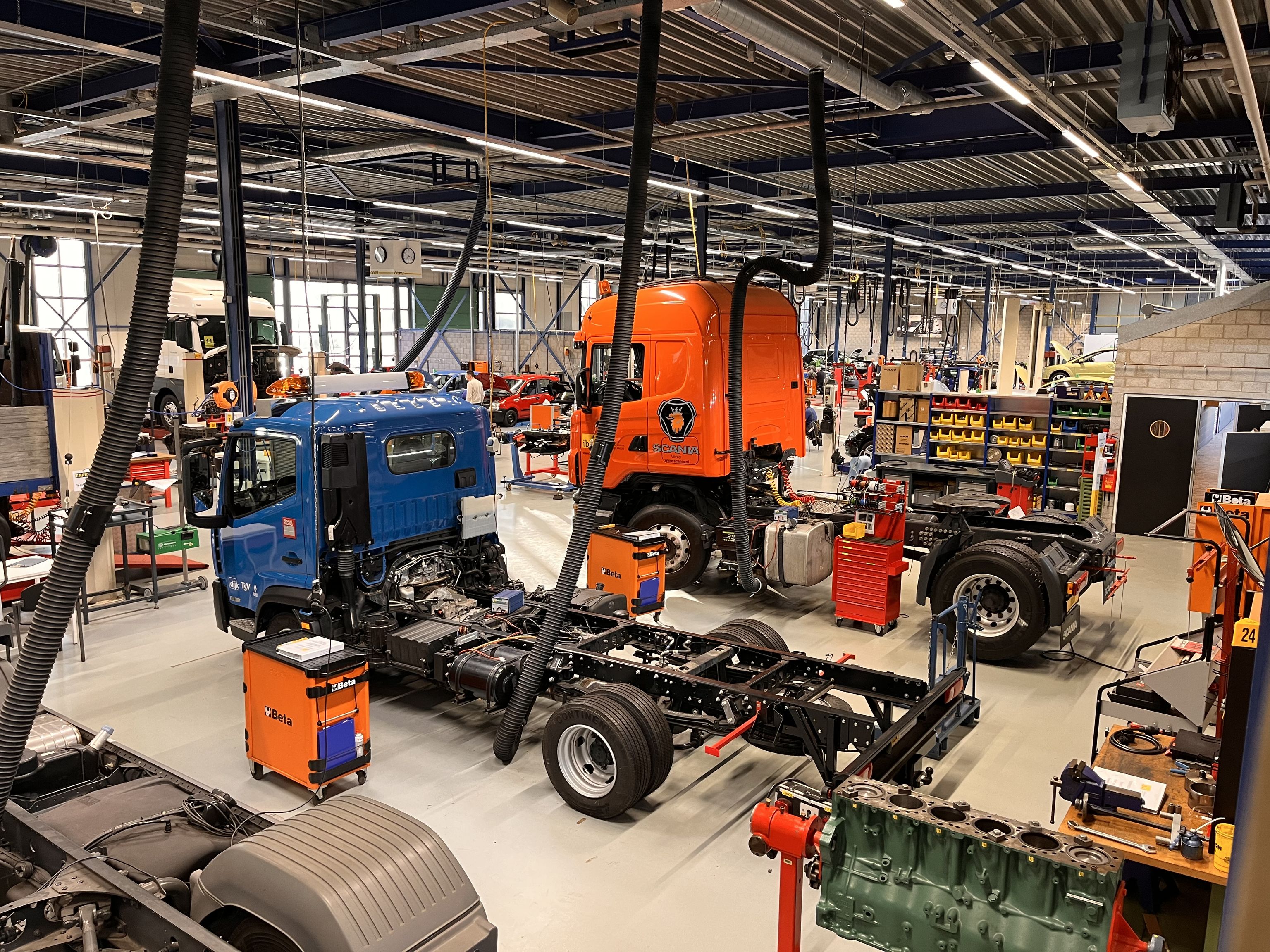 Vrachtauto's zonder oplegger met daarnaast gereedschapskarren in de examenhal. Op de achtergrond bakken met onderdelen.