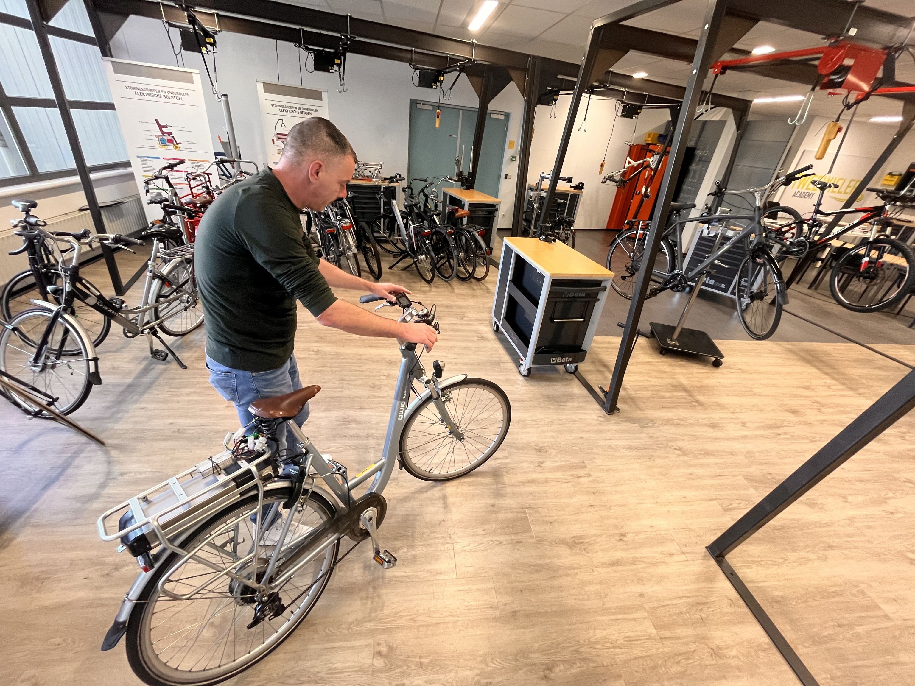 Een man met een elektrische fiets aan de hand in een lokaal met diverse andere fietsen.