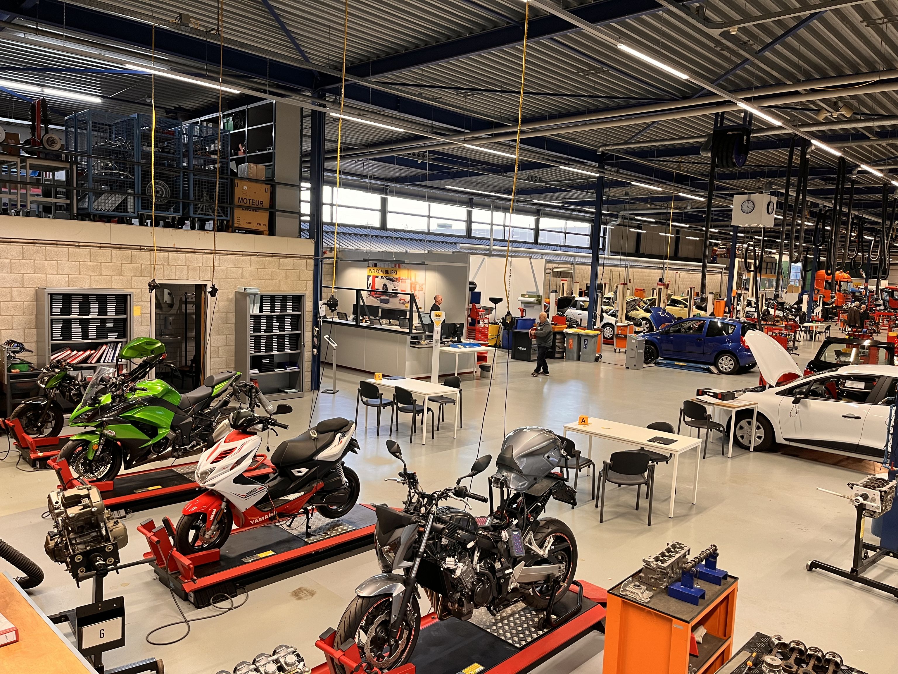 De examenhal van IBKI met motorfietsen op de voorgrond. Daarachter auto's met open motorkap.