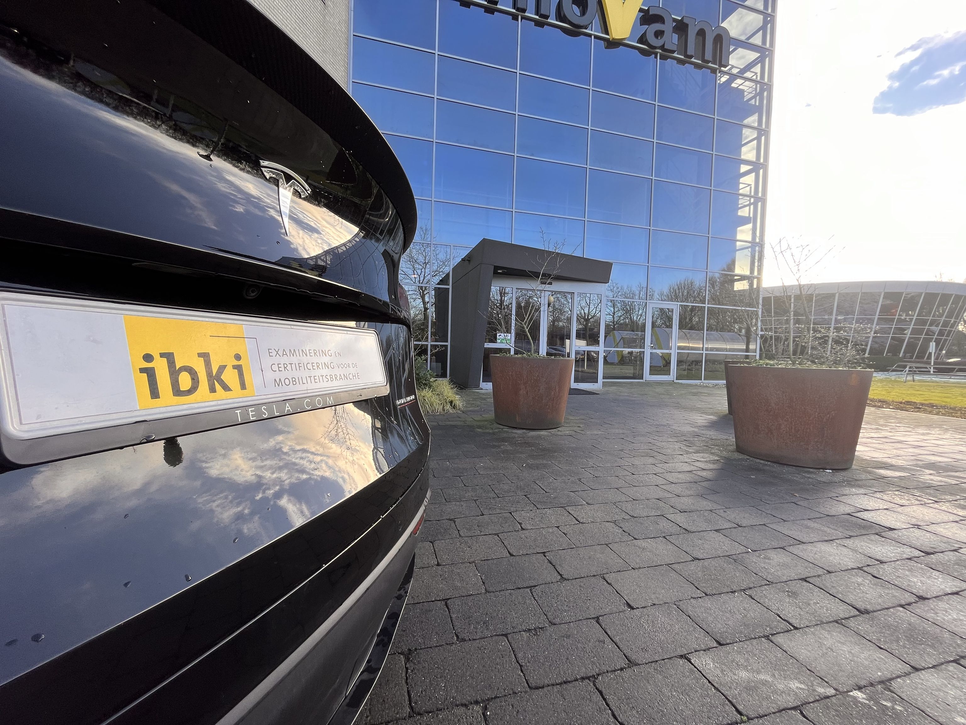 De achterkant van een auto met het logo van IBKI. Daarachter de hoofdingang van de locatie.